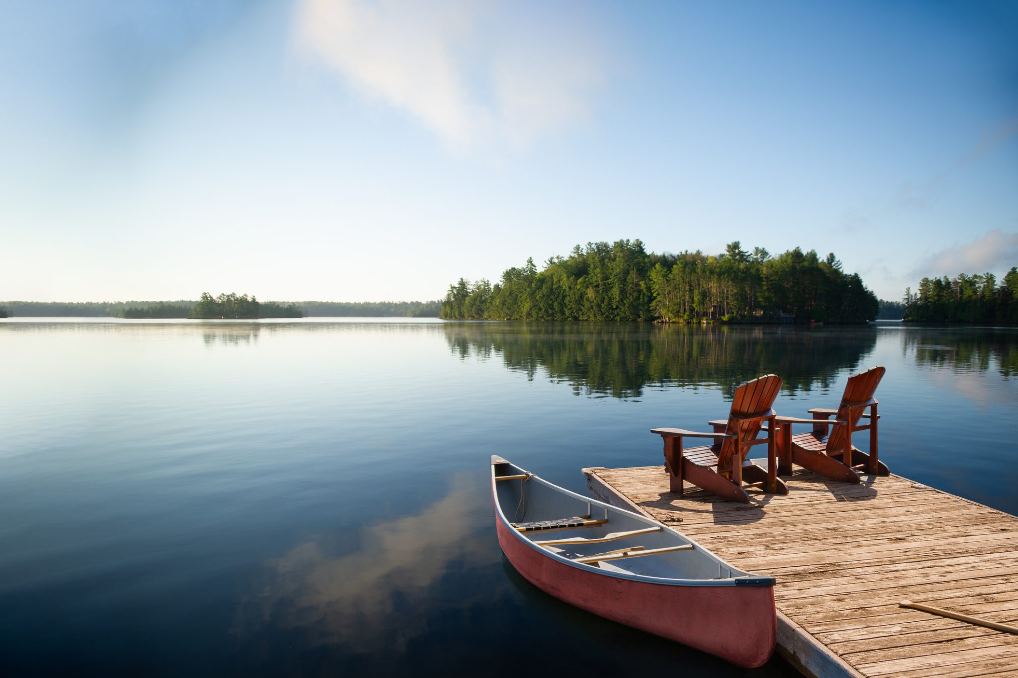 Adirondack chairs on a Muskoka dock with a canoe and lake view.